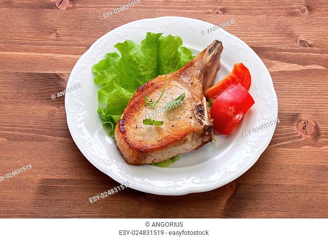 White plate with fried pork cutlet, lettuce and red sweet pepper on the wooden table