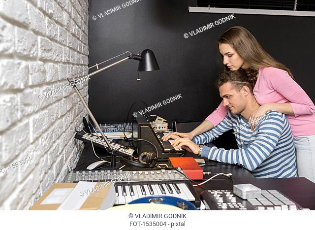 Side view of couple playing synthesizer at table against black wall