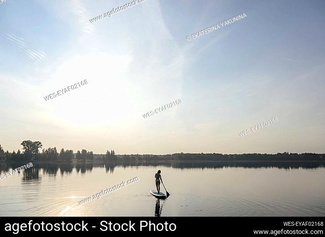 Woman doing standup paddleboarding in lake under sky