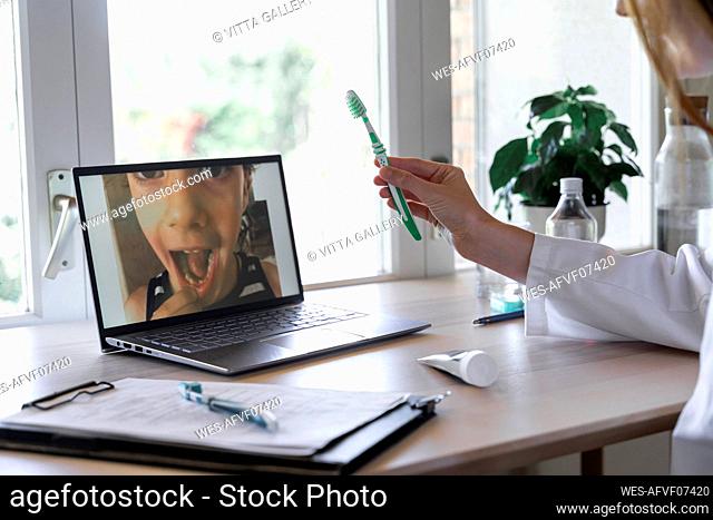 Female dentist showing toothbrush to patient through video call