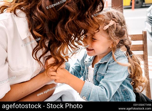 Beautiful mother and young daughter sitting at an outdoor cafe, breakfast day off