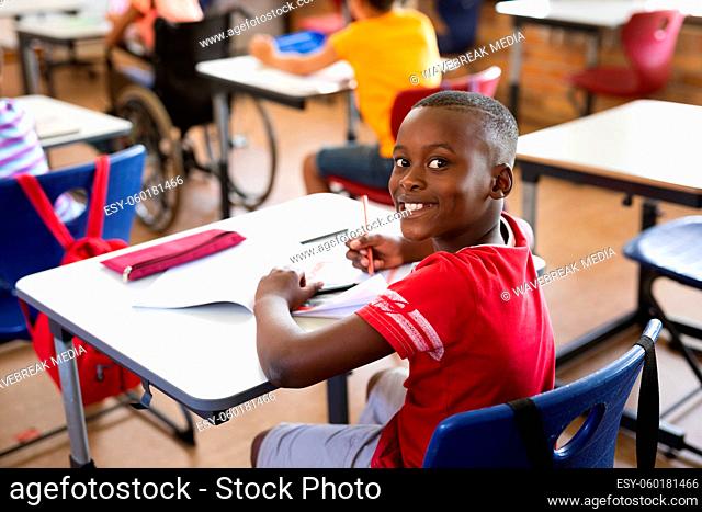 Portrait of african american boy smiling while sitting on his desk in the class at elementary school