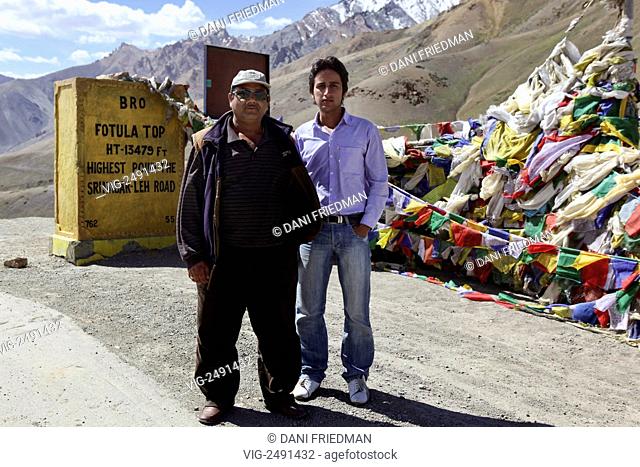 INDIA, FOTULA, 11.07.2010, Two Kashmiri travellers travelling from Srinagar to Leh pose by Buddhist prayer flags at the highest point along the Srinagar-Leh...