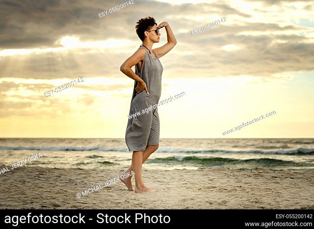 beautiful woman in a gray dress is looking at the sea on the beach at sunset