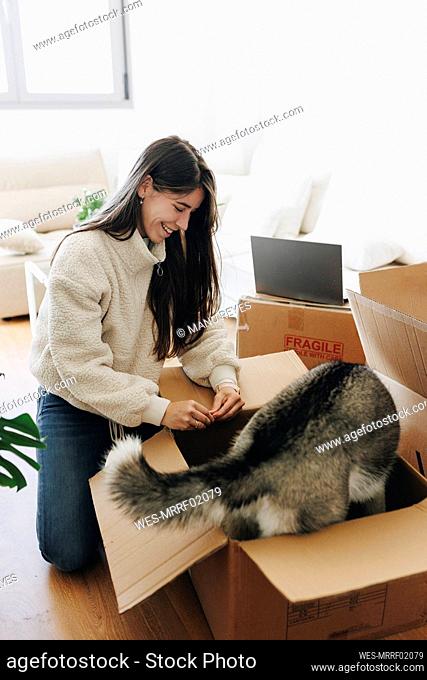 Happy young woman looking at playful dog standing in cardboard box