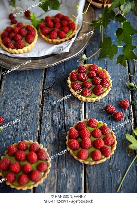 Mini tartes filled with green macha and topped with raspberries lying on blue wooden boards