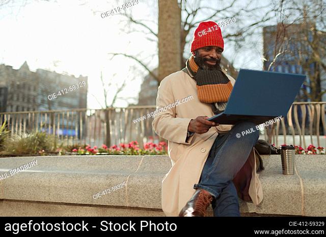 Businessman using laptop in sunny city park