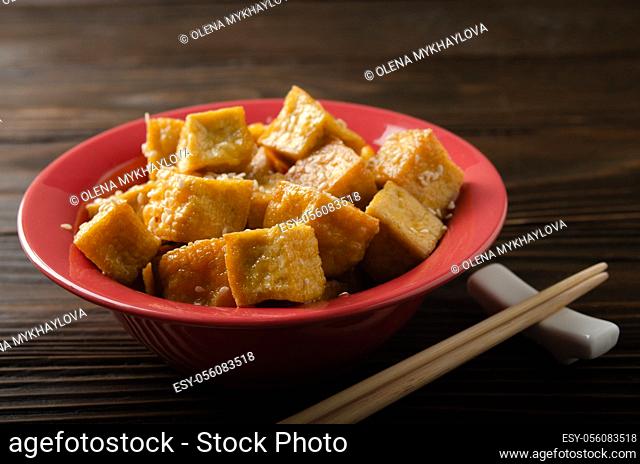 Crispy deep stir fried tofu cubes in clay dish on wooden kitchen table