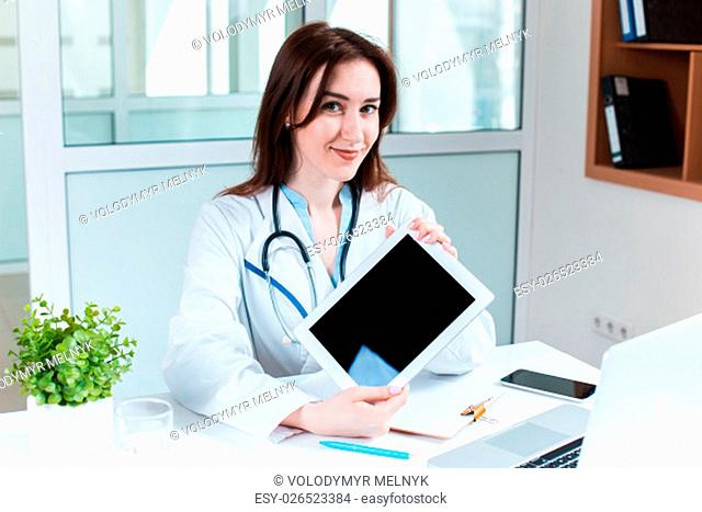 Young pretty woman doctor sitting at the table showing the results on the tablet