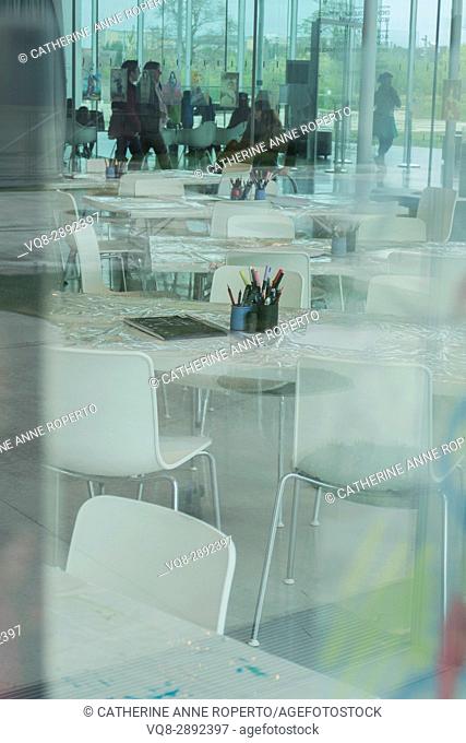 Reflective table coverings and art materials through glass in activity area of contemporary curved glass space with students, Lens, France