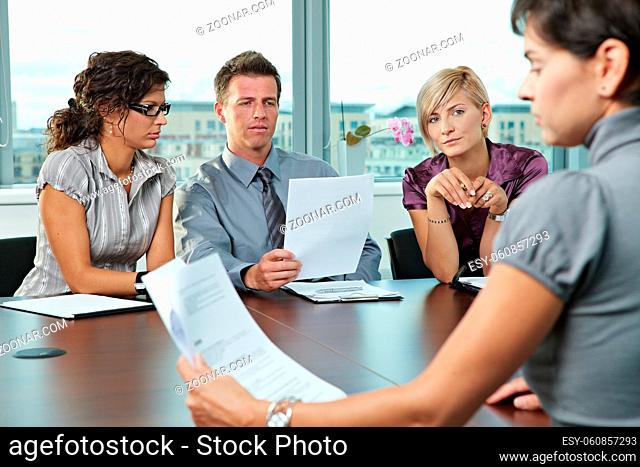 Panel of business people sitting at table in meeting room conducting job interview looking at documents