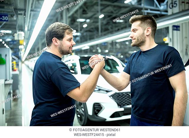 Two colleagues shaking hands in modern car factory