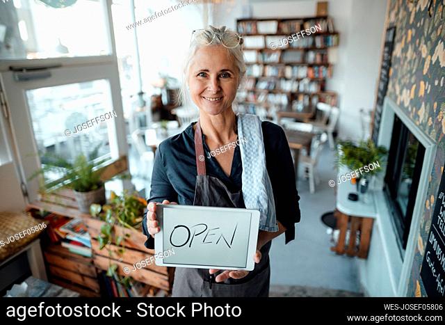 Female entrepreneur holding digital tablet with open text in coffee shop
