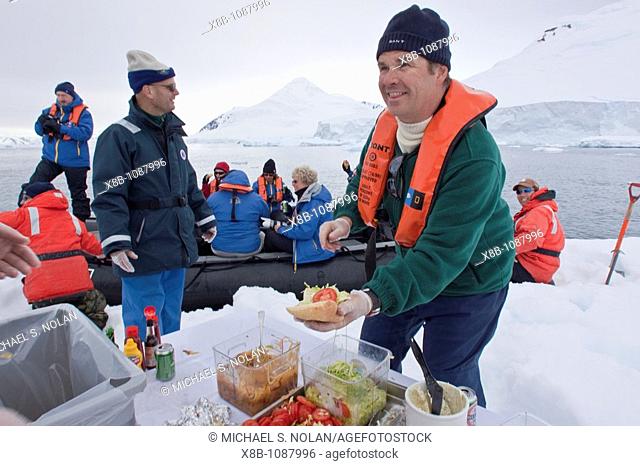 Guests from the Lindblad Expedition ship National Geographic Explorer enjoy a hot asado sandwich prepared by staff at BBQ on an ice floe near Adelaide Island
