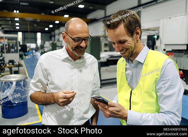 Businessman and man in reflective vest using smartphone in a factory