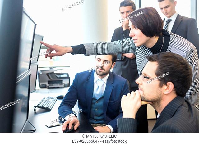Business team looking at data on multiple computer screens in corporate office. Businesswoman pointing on screen. Business people trading online