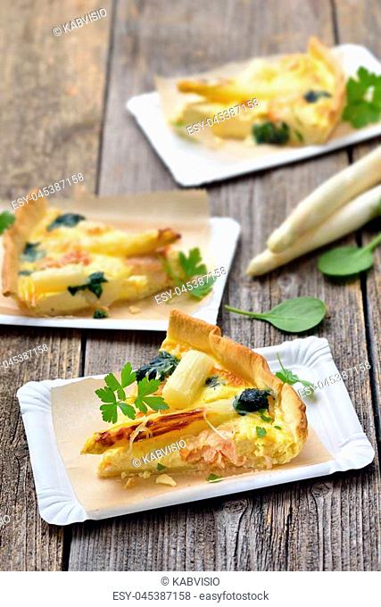 Street food: Slices of fresh quiche with white asparagus, smoked salmon and spinach on paper plates
