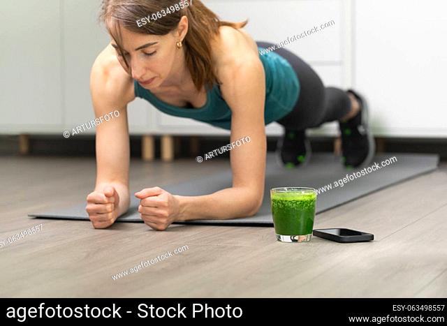 Women doing workout, planking on a gray mat. With smoothie for detox in background. Healthy living, dieting lifestyle
