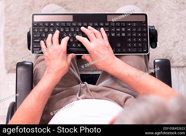 Aged mans hand typing on keyboard. Picture of hands of man who is sitting in wheelchair typing on black computer keyboard taken from above
