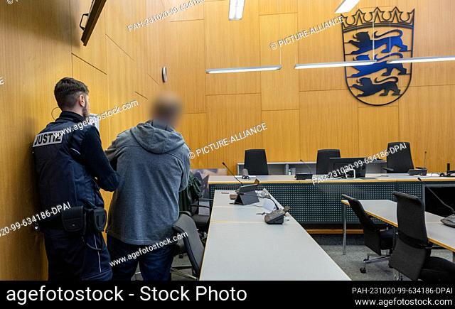 20 October 2023, Baden-Württemberg, Ulm: A judicial constable (l) leads a man to the dock in the regional court at the beginning of a trial for attempted...