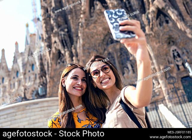 Friends taking selfie through mobile phone standing against Sagrada Familia at Barcelona, Catalonia, Spain