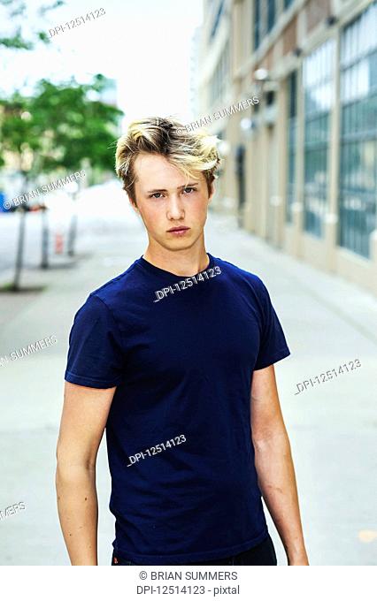 Portrait of a teenage boy wearing a blue t-shirt and standing on a sidewalk in an urban area; Toronto, Ontario, Canada