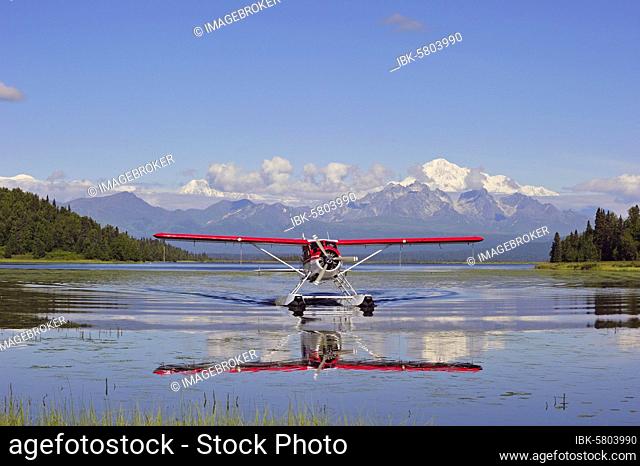 Seaplane Beaver de Havilland lands on a lake off snow-covered mountain Denali, Alaska, USA, North America