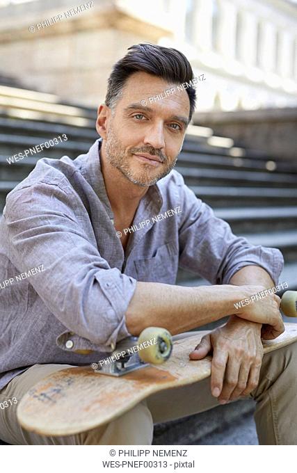 Portrait of relaxed mature man with skateboard sitting on stairs