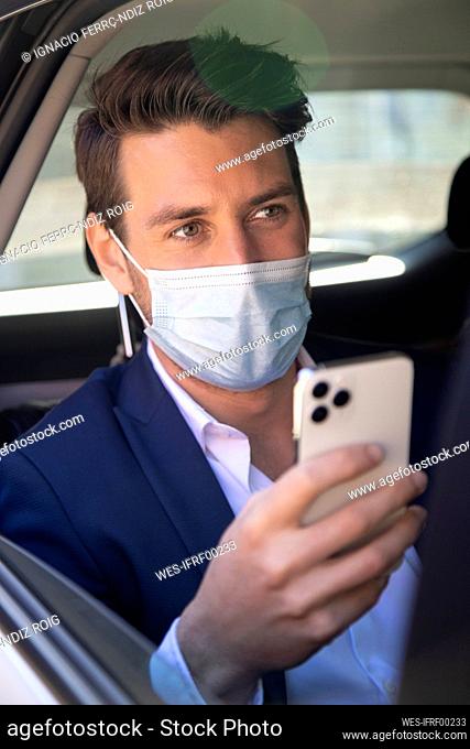 Close-up of businessman wearing mask using smart phone in taxi seen through window