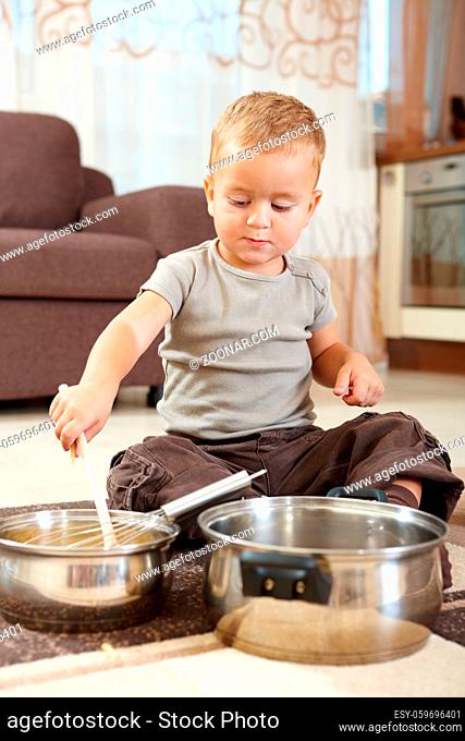 Little boy sitting on carpet in kitchen playing with cooking pots