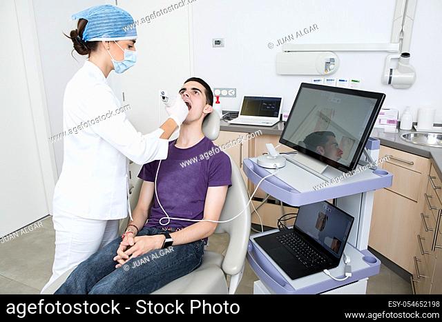Woman in medical uniform using modern tool to make scan of male client teeth during work in dental clinic