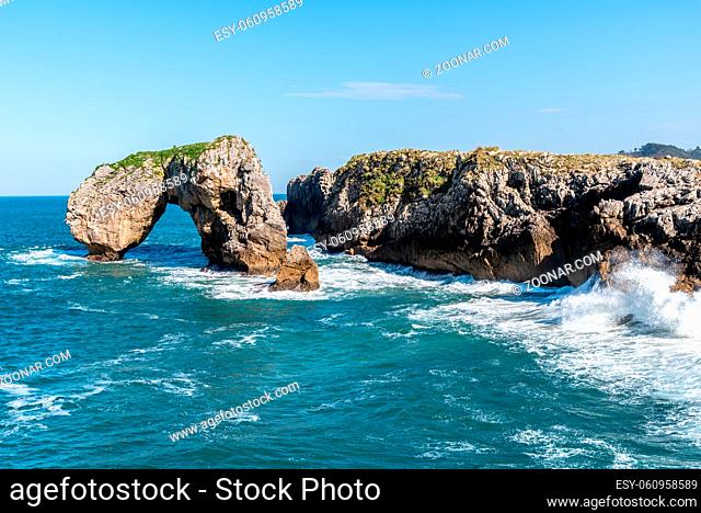 Scenic view of waves splashing against the rocky coast against blue sky. Castro de las Gaviotas, Fort of the Seagulls, and Beach of the Huelga, Llanes, Asturias