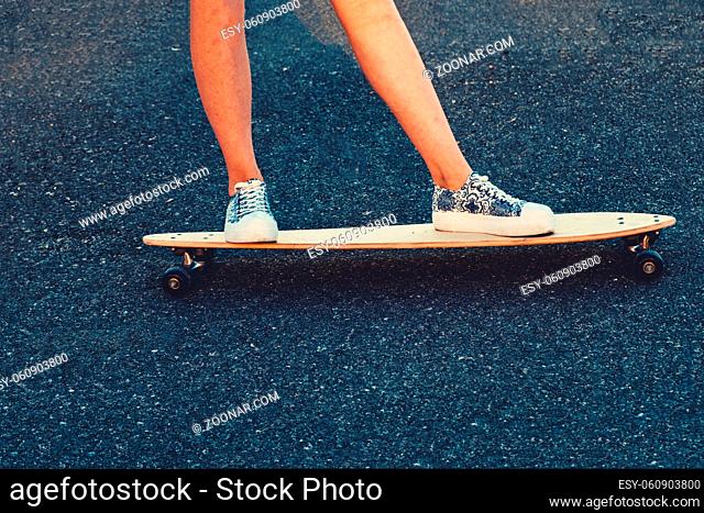 Closeup of skateboarder legs. Woman in sneakers riding skateboard outdoor on asphalt surface. Copyspace on asphalt