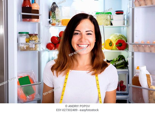 Young Happy Woman With Measuring Tape Standing In Front Of Opened Refrigerator