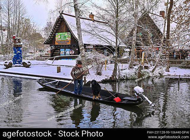 28 November 2023, Brandenburg, Lehde: A man and his dog are walking along a river (waterway) in the snow-covered Spreewald