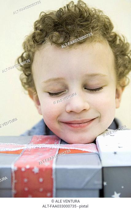Child resting head on gift wrapped boxes, eyes closed and smiling