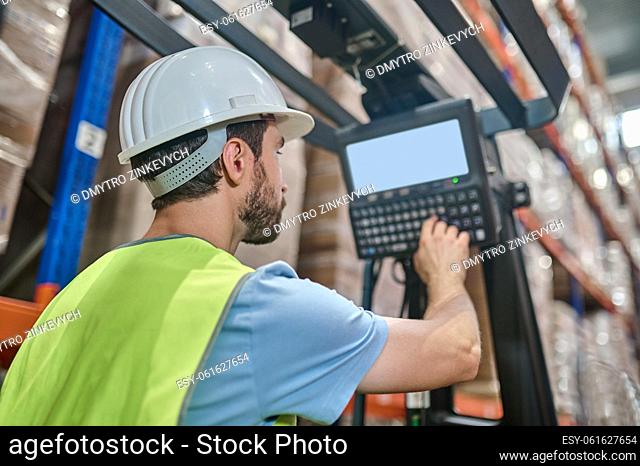Back view of a storehouse worker sitting in the forklift cab and pressing the button on the dashboard panel
