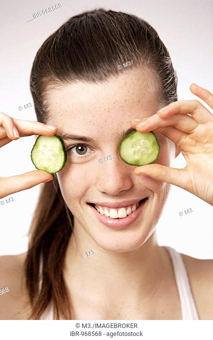 Teenage girl, woman, 17 years-old, holding cucumber slices in front of her eyes, smiling