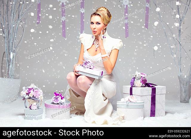Beautiful young bride in felted wedding gown holding present box decorated with purple flowers. Surprise expression
