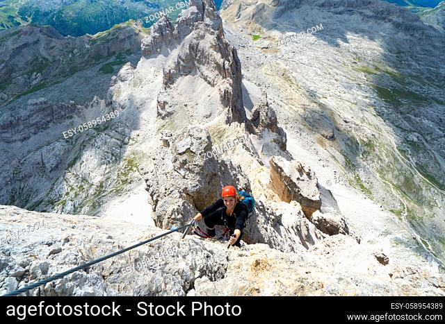 Horizontal view of an attractive blonde female climber on a steep Via Ferrata in the Italian Dolomites with a great view behind