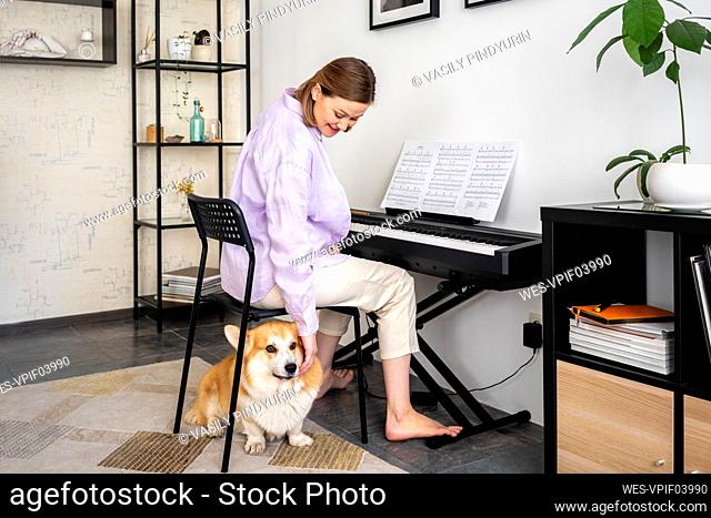 Smiling woman stroking dog while learning piano in living room