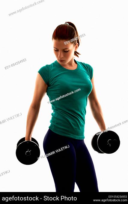 Fit attractive young woman working out with a set of dumbbells, looking down, with a dramatic light, isolated on white background
