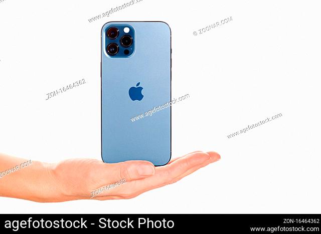 Bratislava, Slovakia - December 07, 2020. Female hand presenting the new iPhone 12 Pro Max Pacific Blue isolated on white background