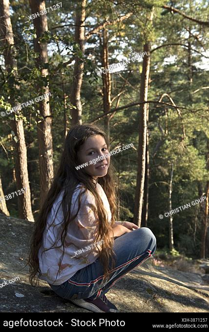 Girl wearing jeans and a shawl, squatting on a flat rock, Rochers d'Angennes site, Forest of Rambouillet, Haute Vallee de Chevreuse Regional Natural Park