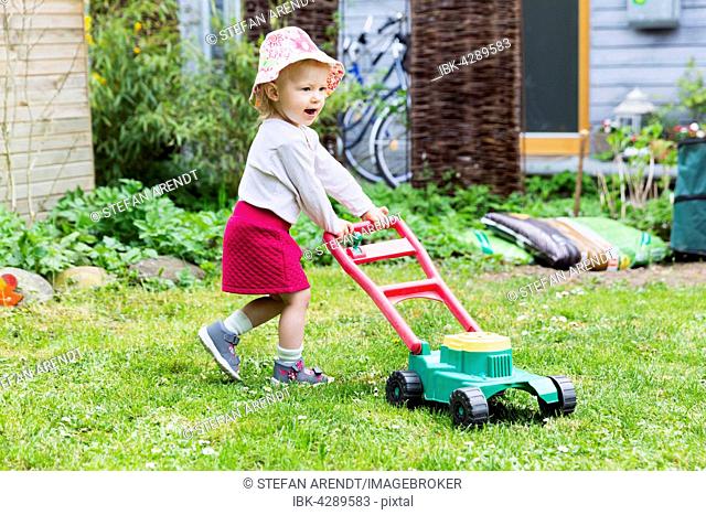 Toddler, little girl in the garden with toy lawn mower