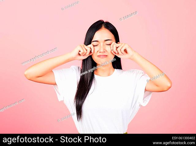 Asian portrait beautiful cute young woman bad mood her cry wipe tears with fingers, studio shot isolated on pink background