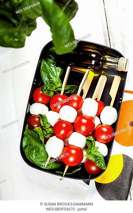 Lunch box of skewered cherry tomatoes and mozzarella cheese balls with basil leaves and vinaigrette