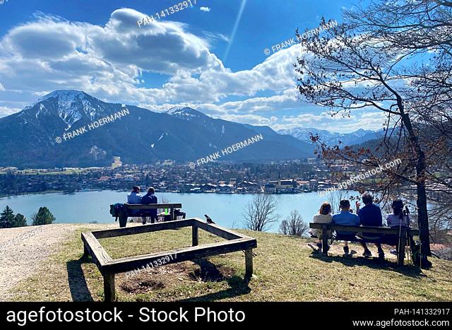 Hikers take a rest on the banks. Hikers on the Hoehenweg over the Tegernsee with a view of Rottach Egern on April 1st, 2021