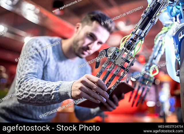 Technician with tablet PC holding robotic arm at workshop
