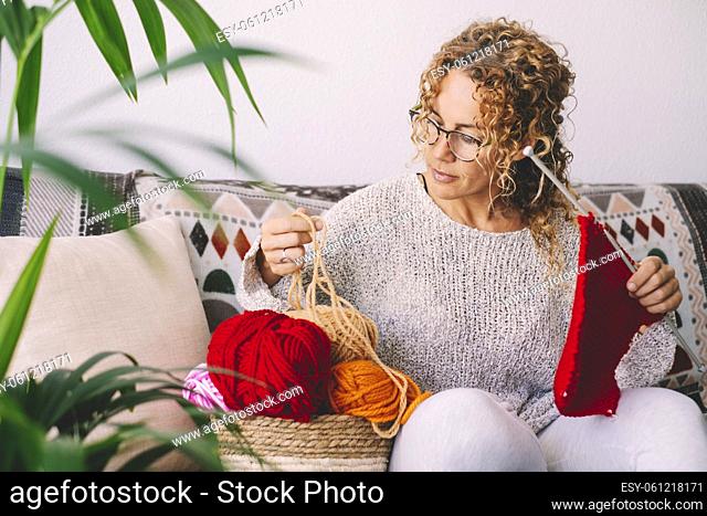 Adult attractive woman at home in knitting work activity using colorful wool. Happy and relaxed female people enjoying time indoor on the sofa